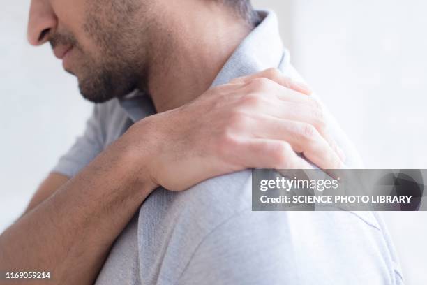 man touching his shoulder in pain - man touching shoulder stock-fotos und bilder
