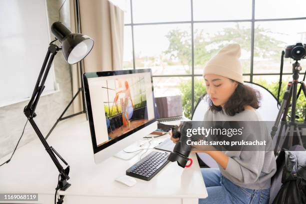 side view of asian female freelancer photographer cheking photos on a digital camera while sitting at the table in workstation - camera girls stockfoto's en -beelden