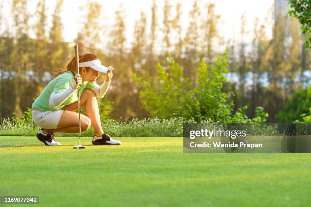 sporty asian woman golf player crouching and study the green before putting shot in vacation and holiday.  sport and healthy concept - putting golf stockfoto's en -beelden