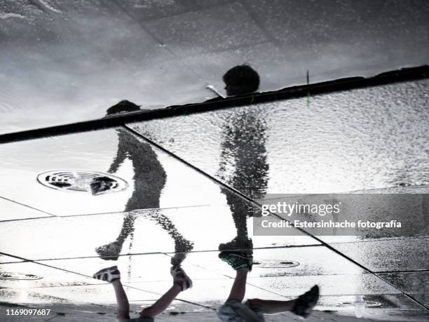 reflection photograph in a puddle of two children playing. - puddle stock pictures, royalty-free photos & images