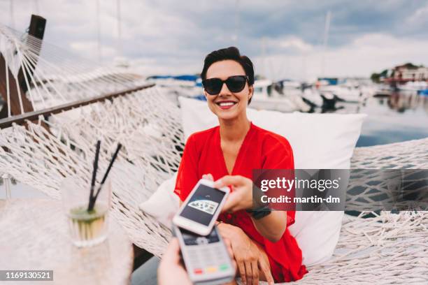 woman at beach cafe paying contactless - nfc payment stock pictures, royalty-free photos & images