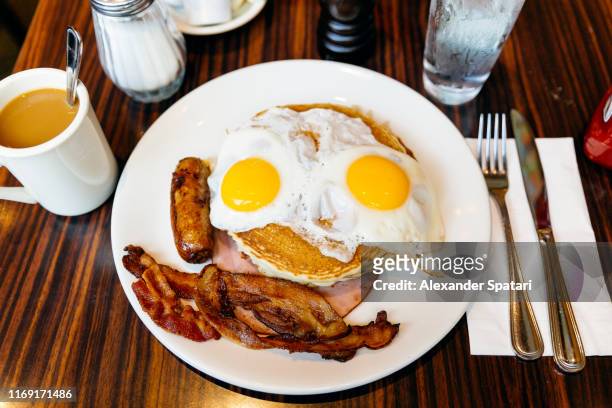 Traditional American breakfast with pancakes, fried eggs, bacon, sausage and ham served in a diner