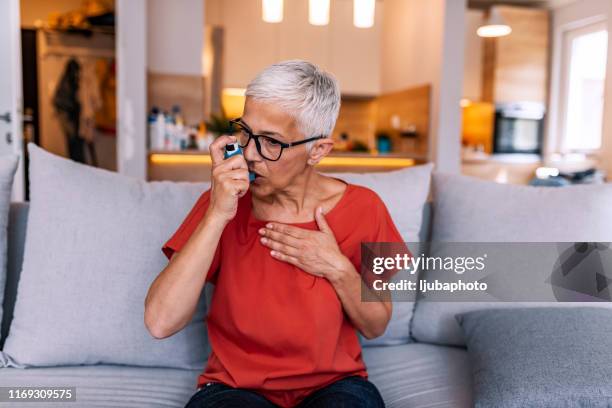 mujer asmática que usa un inhalador - enfermedad crónica fotografías e imágenes de stock