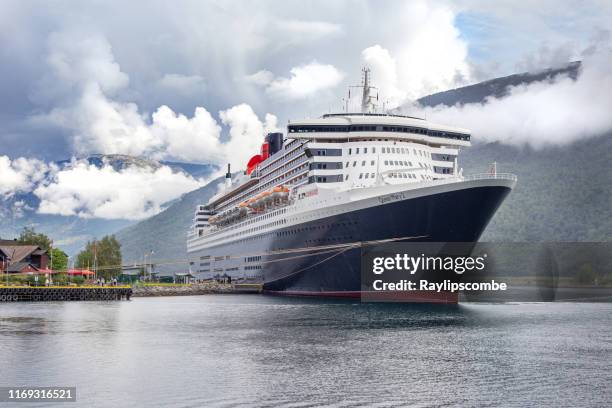 cunardのオーシャンライナーと旗艦、クイーンメアリー2は、周囲の山の風景の上に低くぶら下がっている雲に囲まれたノルウェーのフィヨルドのフラムの見事な会場にドッキングしました。 - rms クイーン メアリー 2 ストックフォトと画像