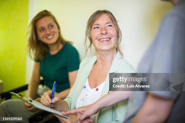 woman signing a form at medical office - seguro médico fotografías e imágenes de stock