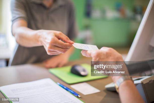 receptionist giving a health card to female patient at clinic - krankenversicherung stock-fotos und bilder
