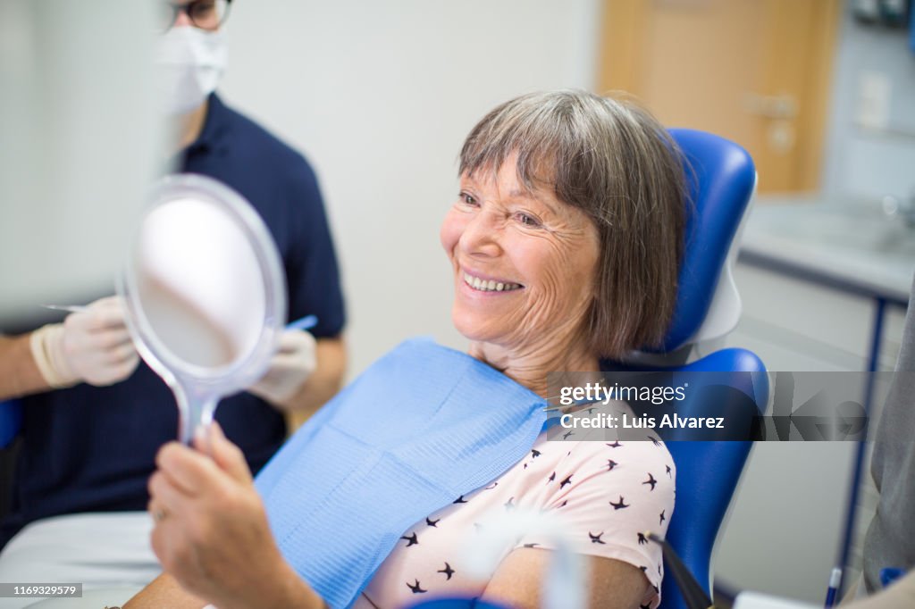Senior woman looking at mirror with smile in dentist’s office