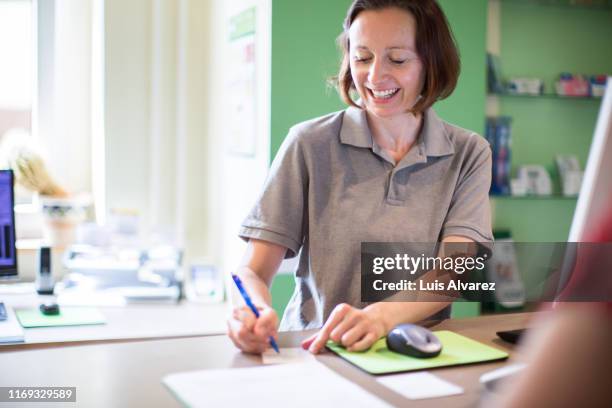 smiling clinic receptionist making a health card for a patient - dental office - fotografias e filmes do acervo