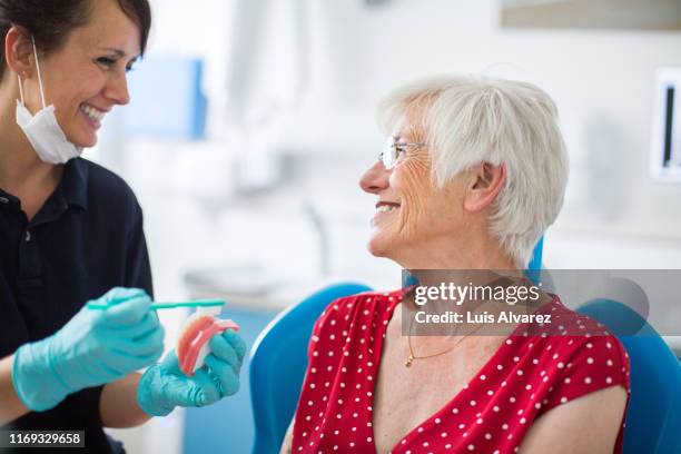 dentist showing her patient how to brush teeth at clinic - blauer handschuh stock-fotos und bilder