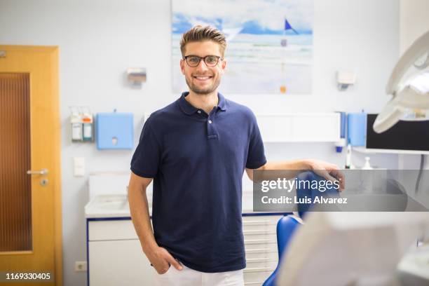 confident male dentist standing in his clinic - polohemd stock-fotos und bilder