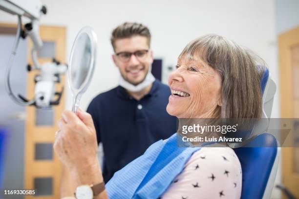 senior patient checking her teeth after treatment - dentist's office fotografías e imágenes de stock