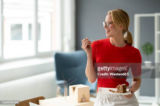happy young woman eating a piece of cake in office - model eating stock pictures, royalty-free photos & images