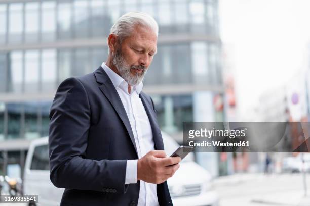 mature businessman using cell phone in the city - mann anzug gebäude objekt draussen stock-fotos und bilder