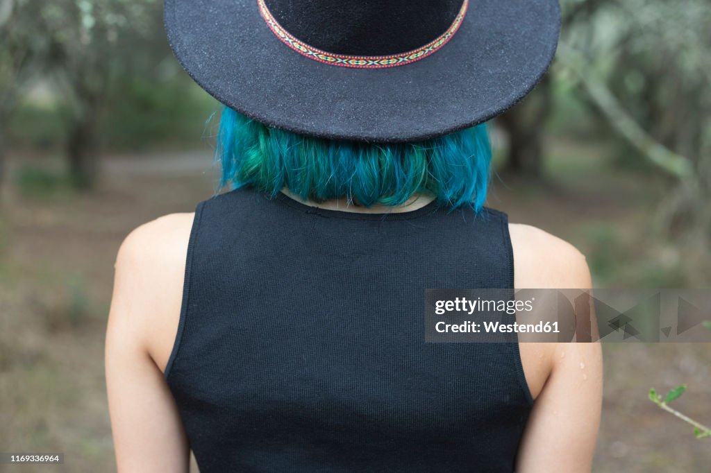 Back view of young woman with dyed blue and green hair wearing black hat