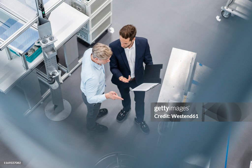 Two businessmen with clipboard talking in a factory