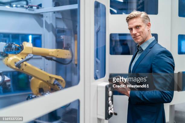 portrait of a confident businessman in front of a robot in a modern factory - 40 44 years blond hair mature man factory stock pictures, royalty-free photos & images