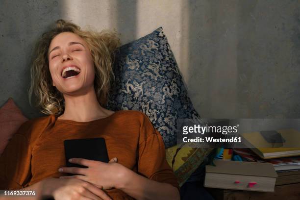 portrait of laughing young woman lying on bed with e-book reader - e reader stock-fotos und bilder