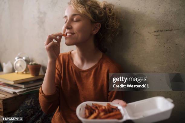 portrait of young woman eating french fries at home - fries foto e immagini stock