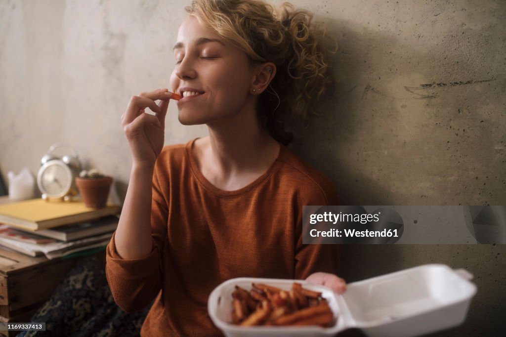 Portrait of young woman eating French Fries at home