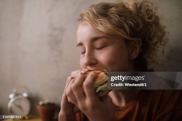 portrait of young woman eating hamburger - consume photos et images de collection