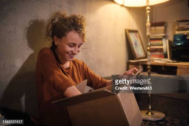 smiling young woman unpacking parcel at home - floor lamp stock-fotos und bilder