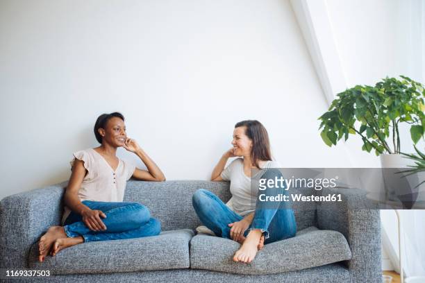 two relaxed women sitting on couch at home talking - couple lifestyle jean stock pictures, royalty-free photos & images