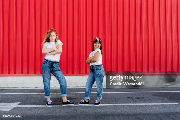 sisters with arms crossed standing in front of a red wall - kids standing crossed arms stock pictures, royalty-free photos & images