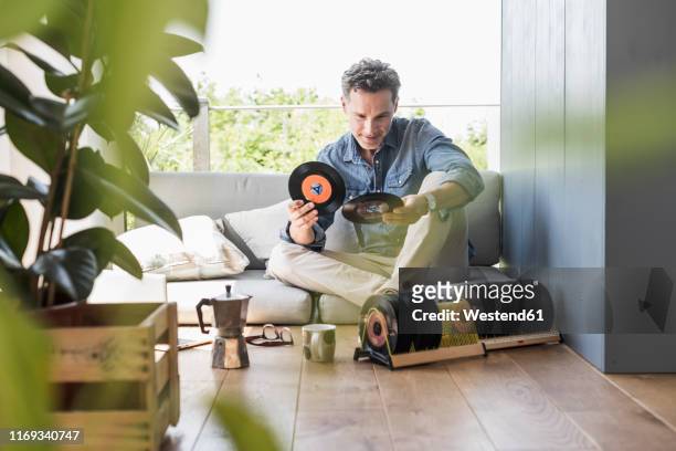 mature man sitting at home, looking at vintage sigle recors - freizeit stock-fotos und bilder