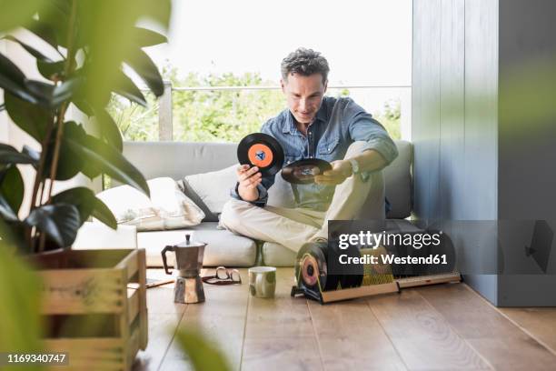 mature man sitting at home, looking at vintage sigle recors - collection foto e immagini stock