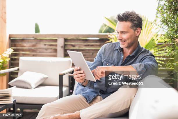 mature man sitting on terrace, using digital tablet - garden ipad stock pictures, royalty-free photos & images