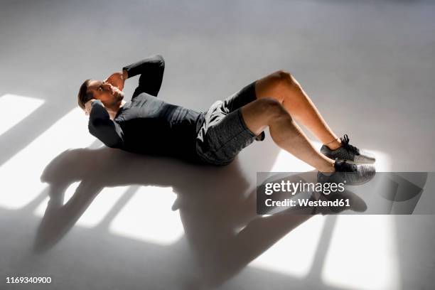 athlete doing crunshes in sunlit studio - sit up foto e immagini stock