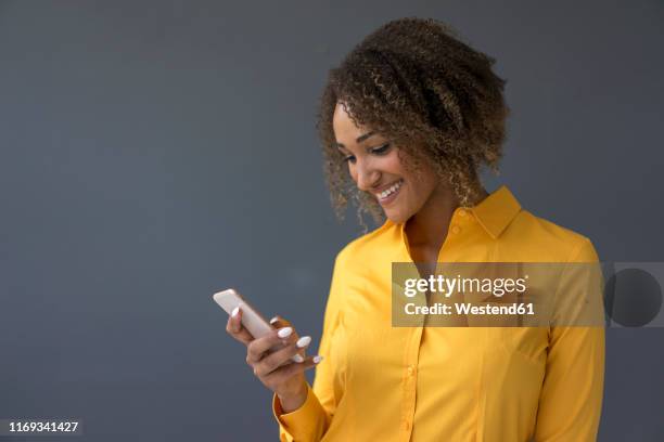 portrait of smiling young woman wearing yellow shirt looking at cell phone - yellow shirt stock pictures, royalty-free photos & images