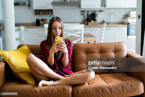 young woman using cell phone on a couch at home - 'woman on couch stock pictures, royalty-free photos & images