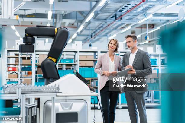 businessman and businesswoman in a modern factory hall looking at robot - digitization stockfoto's en -beelden