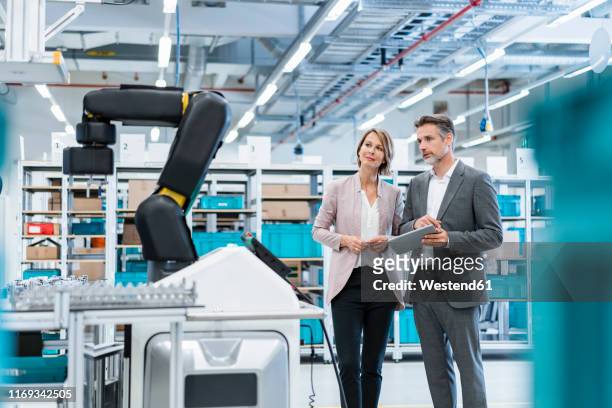 businessman and businesswoman in a modern factory hall looking at robot - digitalization stock pictures, royalty-free photos & images