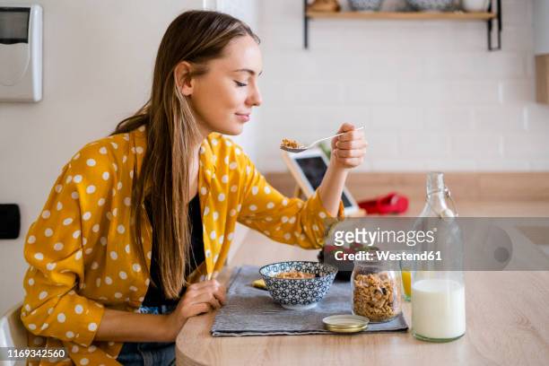 young woman enjoying breakfast in kitchen at home - breakfast cereal fotografías e imágenes de stock