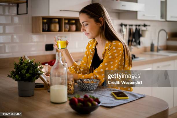 young woman using tablet and having breakfast in kitchen at home - yellow milk stock-fotos und bilder