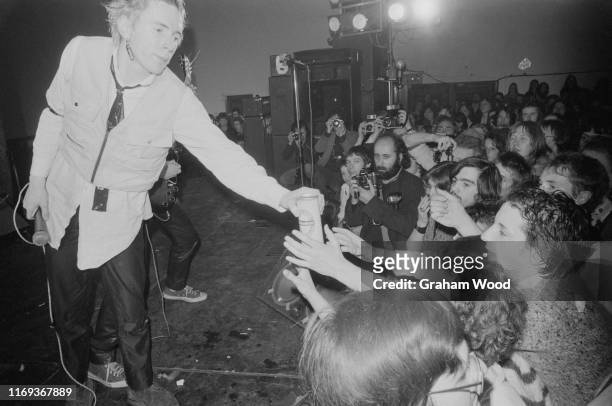 English singer Johnny Rotten of punk rock band The Sex Pistols hands a can of beer to fans while on stage at Leeds Polytechnic during their 'Anarchy...