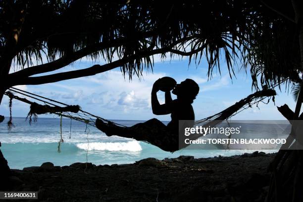 Bob Lisale drinks coconut milk as he watches the king tides pound the coast of Funafuti Atoll, 19 February 2004, home to nearly half of Tuvalu's...