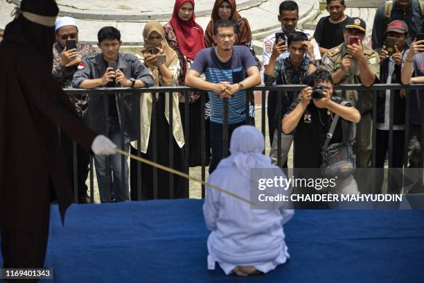 People watch as a woman is whipped in public by a member of the Sharia police in Banda Aceh on September 19, 2019. - A trio of canoodling couples...