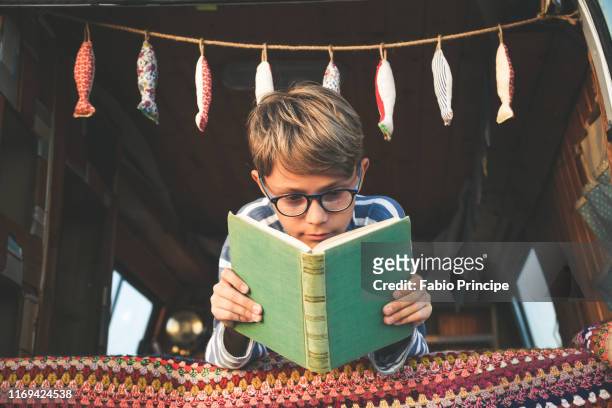 low angle view of boy reading book - reading fotografías e imágenes de stock