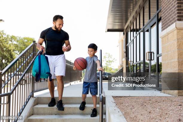 young boy with basketball leaves gym after game with dad - sports centre exterior stock pictures, royalty-free photos & images