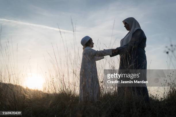 muslim mother and son silhouette on sunset meadow - arab woman silhouette stock pictures, royalty-free photos & images