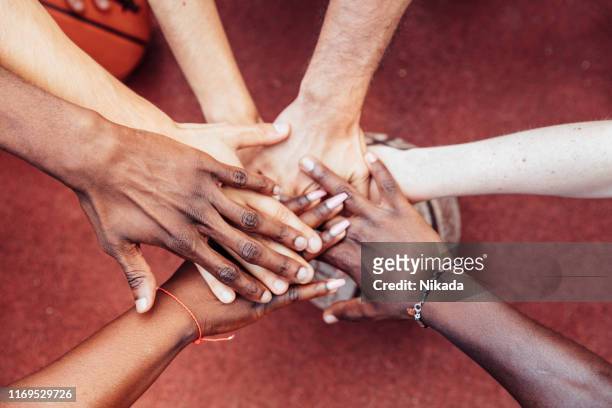 high angle view of male and female friends stacking hands over basketball at court - hand stack stock pictures, royalty-free photos & images