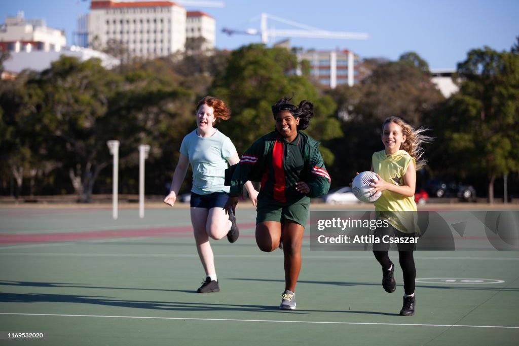 Smiling teenage girls running with ball on sunny sport field