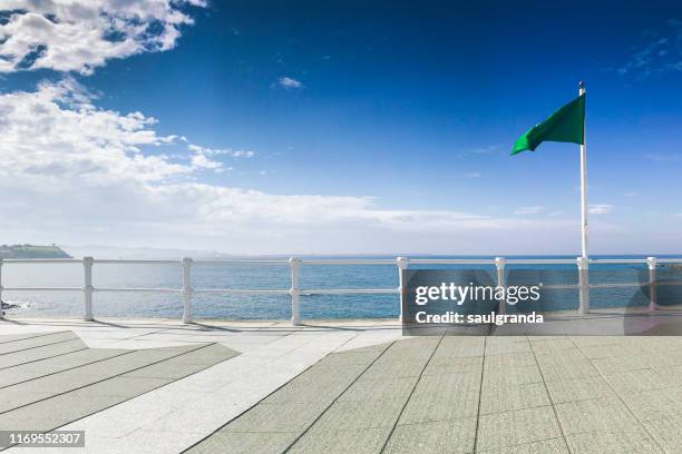 a green flag weaving against the sea - promenade seafront stock pictures, royalty-free photos & images