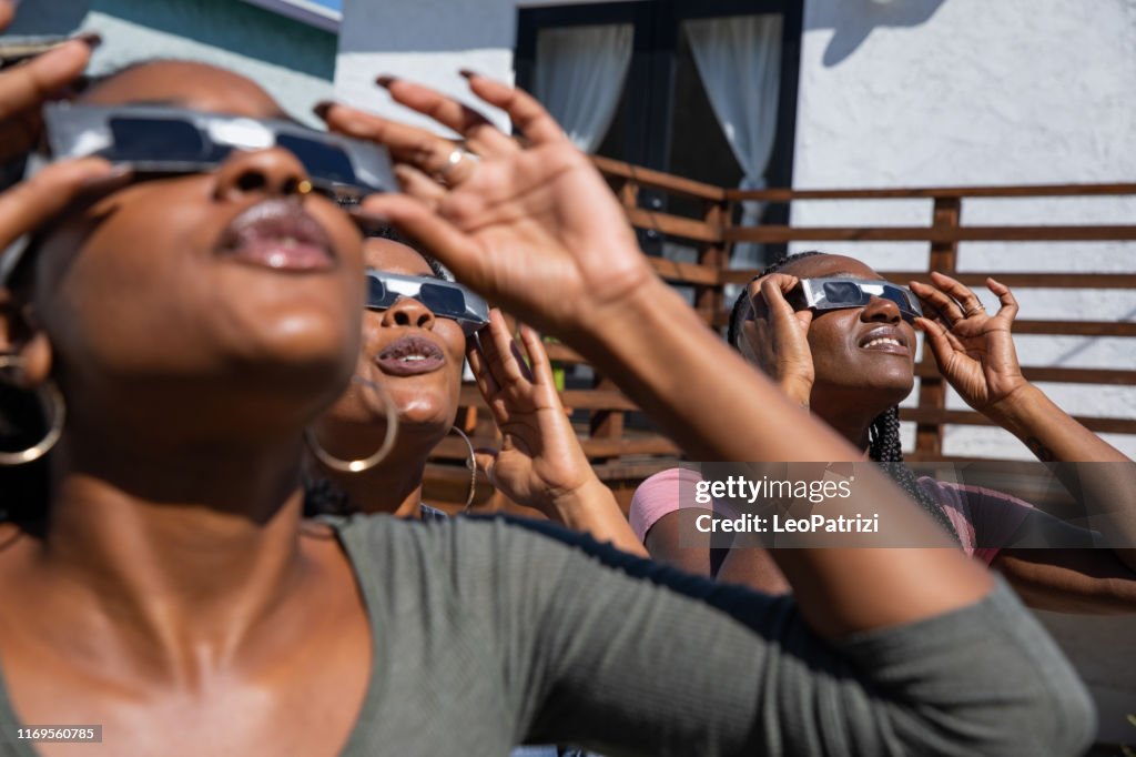 Women friends at home enjoying solar eclipse looking at the sun with eclipse sunglasses