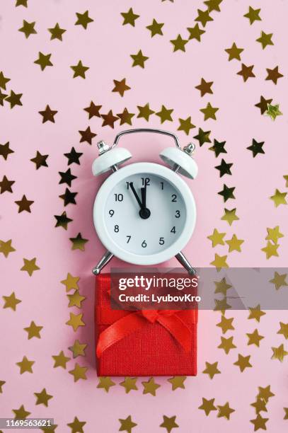 white alarm clock with red gift and star confetti on pink delicate background for holiday time. - star confetti white background stockfoto's en -beelden