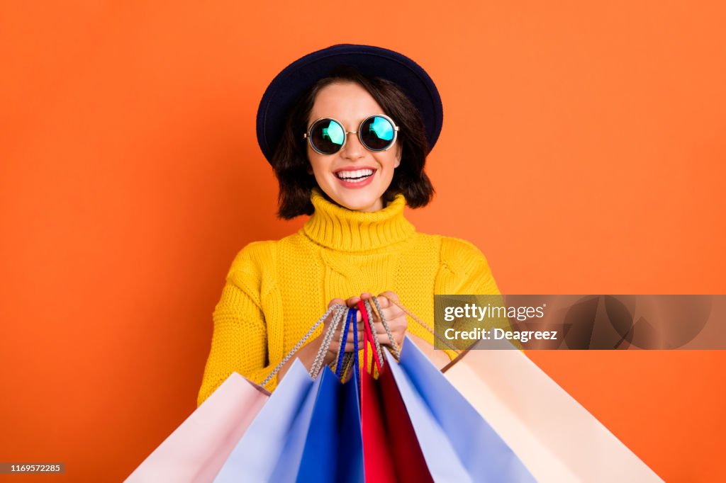 Photo of shopping cheerful girl wearing cap showing you what she has bought while isolated with orange background