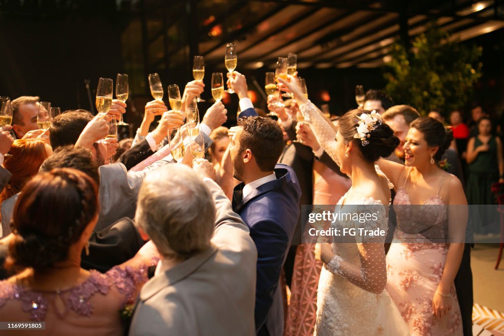 Novia, novio e invitados de boda haciendo un brindis